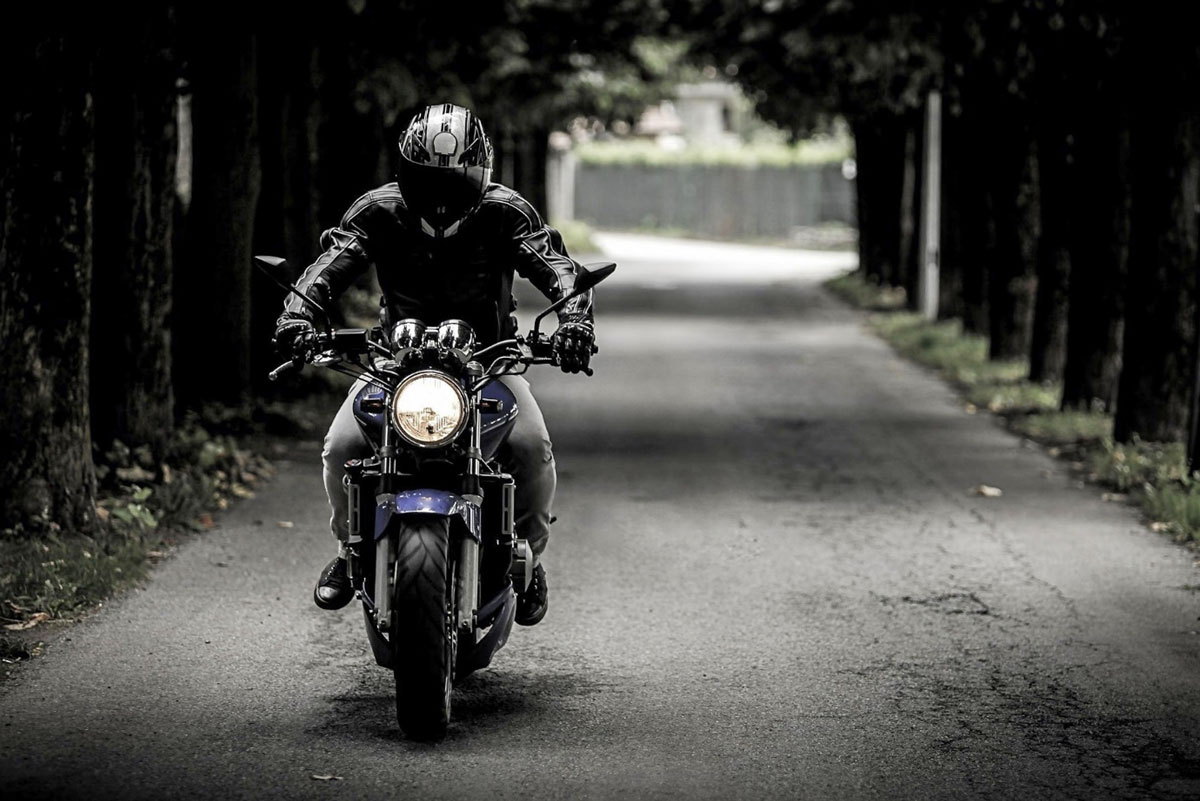 motorrad schwarz gekleideter Biker auf einem Motorrad, fährt eine einsame Straße entlang